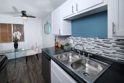 1550 apartments kitchen in Las Vegas, 89119. White cabinets with modern silver pulls, dishwasher, and grey tone tile backsplash.
